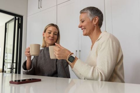 Mother and daughter clinking mugs in modern white kitchen, morning coffee bonding moment