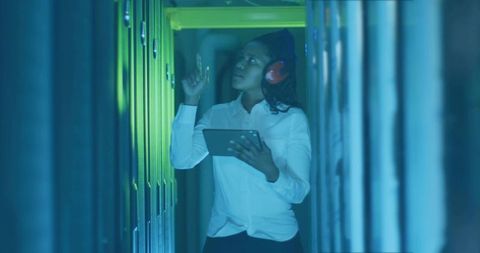 Female it technician inspecting server room with tablet and earmuffs