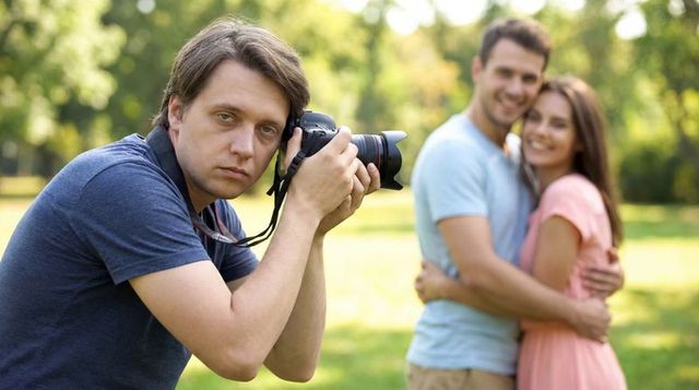 Dslr photographer capturing smiling couple embracing in sunlit park with soft bokeh