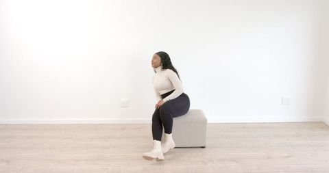 Woman Sitting on Ottoman in Minimalist White Room Thinking