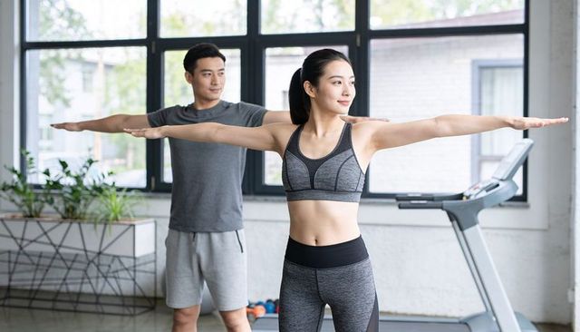 Couple stretching together in bright modern gym, woman holding extended arm pose