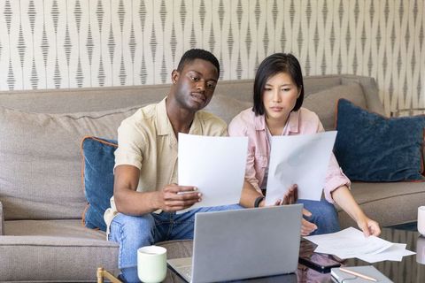 African american and korean couple reviewing bills and budgeting on laptop at home