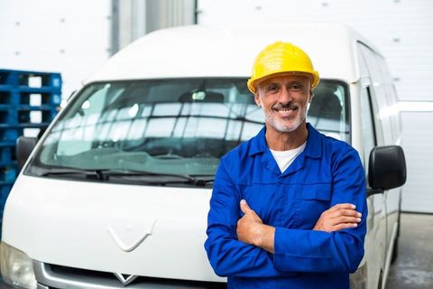 Confident warehouse worker in safety gear standing by delivery van