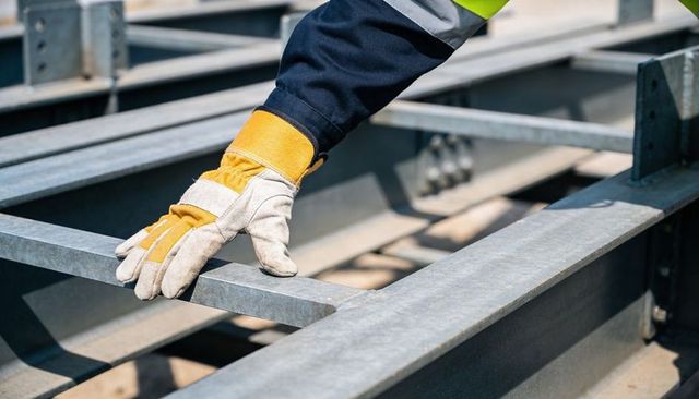 Worker inspecting galvanized steel beams with leather safety glove and hi-vis sleeve