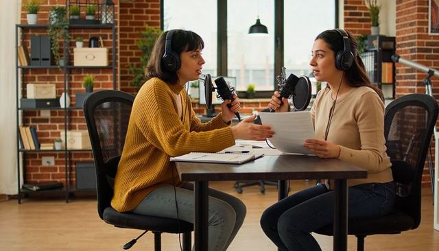 Two Women Recording Podcast in Loft Studio Discussing Script with Microphones