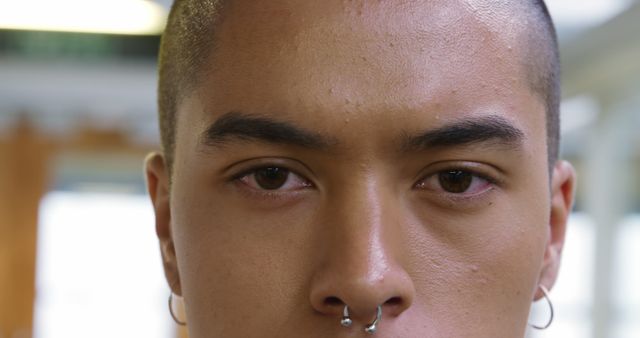 Close-up of a young biracial man with a nose piercing, with copy space. His confident gaze suggests a strong personality and individual style.