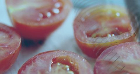 Macro halved tomatoes sitting cut-side-up on baking mat closeup glossy juices and seeds