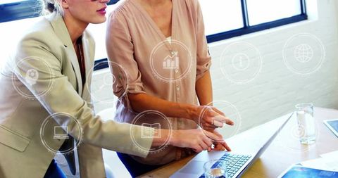 Colleagues collaborating over laptop with digital hud icons in modern sunlit office