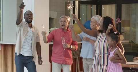 Diverse multi-generational family celebrating with sparklers on covered patio toasting