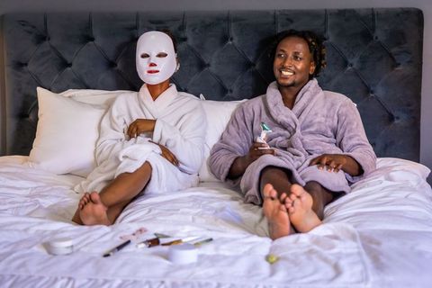 African american couple enjoying led face mask and handheld skincare device in robes