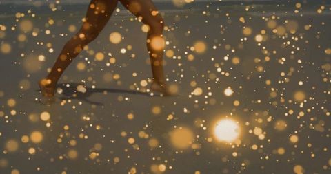 Barefoot woman walking on wet shoreline at sunset with golden bokeh glow
