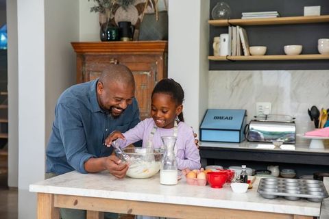 African american father and daughter baking together in home kitchen stirring batter and smiling