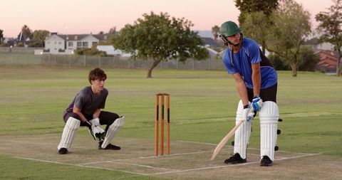 Sunset suburban cricket practice with batsman and wicketkeeper, wooden bat, orange stumps