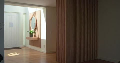 Sunlit wooden console and round mirror on slatted wall in minimalist modern foyer
