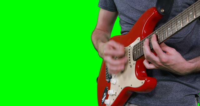 Mid section of male musician playing guitar against green screen