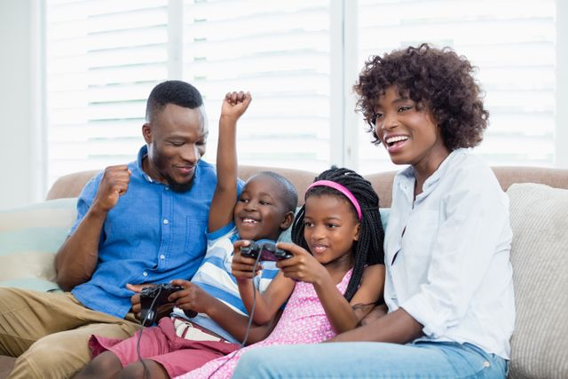 African American family enjoying quality time playing video games together in living room. Perfect for articles on family bonding, technology in family life, or advertisements for gaming consoles and family-friendly games.