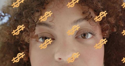 Curly-haired woman gazing through orange dollar-sign overlays, closeup portrait