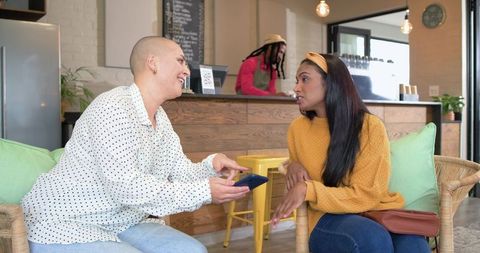 Diverse friends chatting and sharing smartphone in cozy urban cafe, mustard sweater