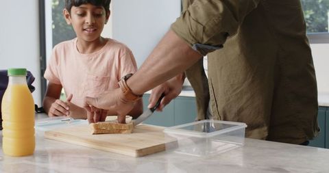 Father and son slicing sandwich on kitchen table