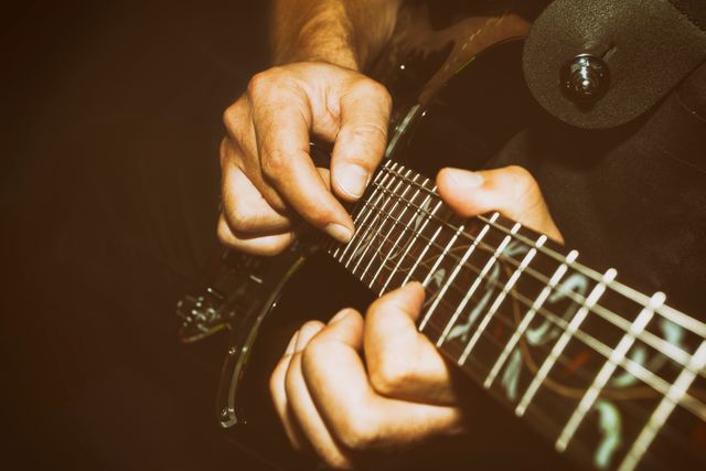 Close-up view of a musician's hands skilfully playing an electric guitar, focusing on the hands and guitar strings. Ideal for advertising music schools, guitar tutorials, musical events, or articles on musicianship and guitar techniques.
