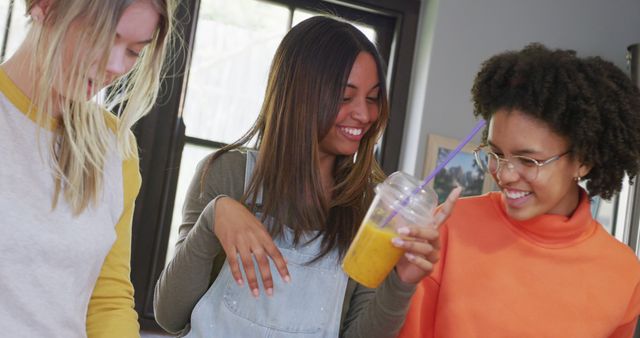 This vibrant image shows three young women enjoying their time together in a kitchen, each smiling and engaged with one another. The relaxed and cheerful atmosphere is perfect for use in advertisements, social media campaigns, or blog articles focusing on friendship, healthy living, and community.