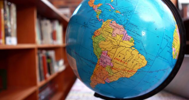 Image showing close-up of a globe highlighting South America positioned beside a bookshelf filled with books. Ideal for educational material, geography presentations, travel blogs, research publications, and classroom resources that promote global awareness and learning.