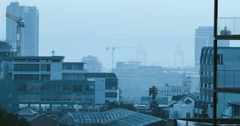 Balcony framing mid-rise buildings with crane and port cranes over hazy waterfront skyline