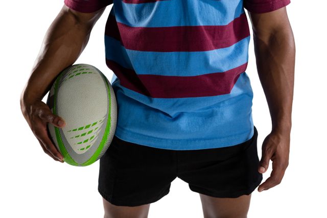 Mid section of male player holding rugby ball while standing against white background
