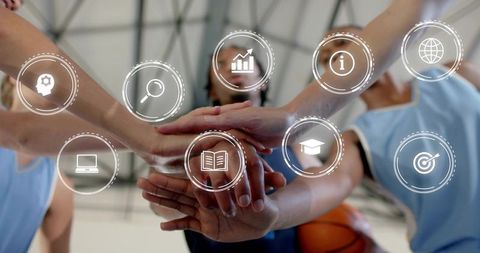 Basketball team stacking hands in gym with digital icons overlay representing teamwork