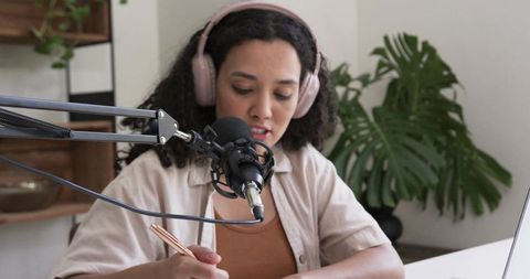 African american creator recording podcast at home wearing pink headphones and using laptop
