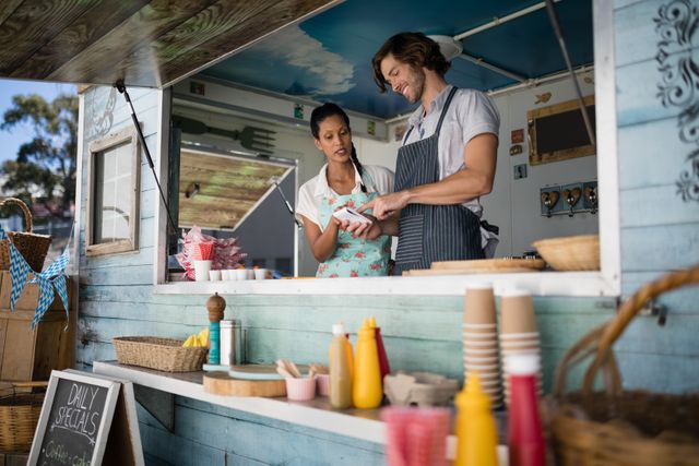 Food truck staff discussing orders at the counter. Useful for themes related to small businesses, street food, customer service, teamwork, and outdoor dining.