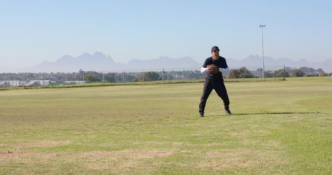 Mature man holding football on suburban grass field with mountain horizon and copy space