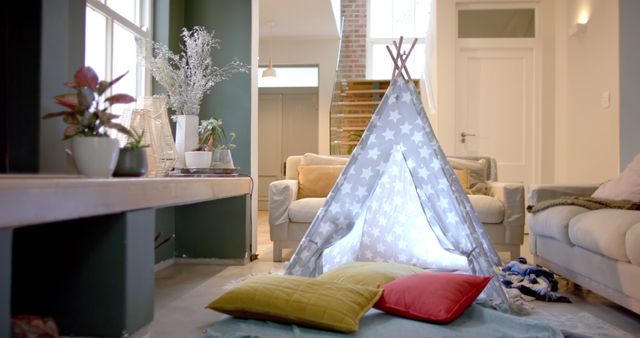 A cozy play tent adorned with star patterns is set up in a modern living room. The tent is filled with light and surrounded by colorful cushions, creating a inviting children's play area. Stylish furniture, including a white couch and plants, adorn the space. This image can be used for articles about home decoration, creating comfortable play areas for children indoors, or showcasing family-friendly living room designs.