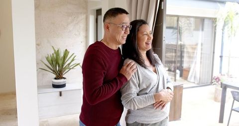 Senior couple standing by glass door enjoying patio view at home