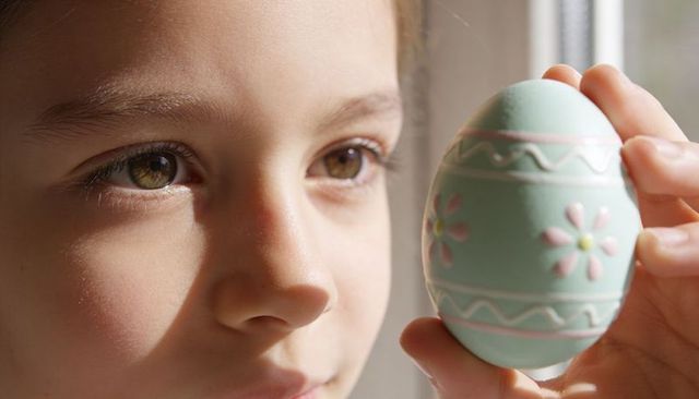 Gazing child holding pastel decorated easter egg closeup sunlit portrait tender keepsake