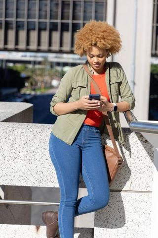 African american woman leaning on urban overpass texting on smartphone in casual denim