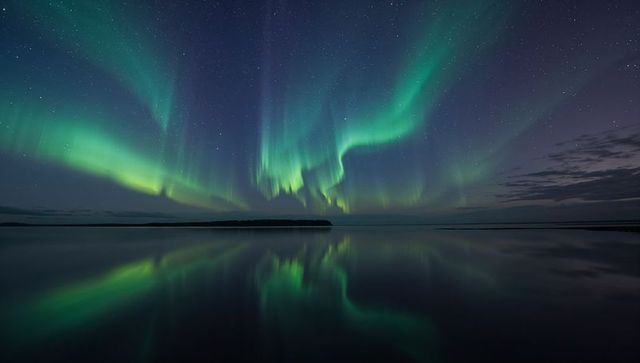 Dancing green aurora reflecting over calm lake under starry night sky
