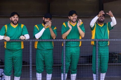 Cricket teammates cheering and clapping from dugout in green and yellow uniforms