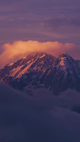 Vertical sunrise revealing snow-capped alpine peak while golden cloud drifting across sky