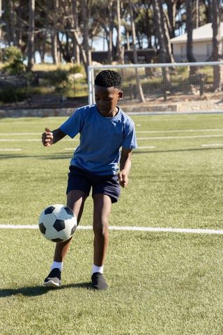 Young boy practicing soccer juggling on sunny grass field with goal in background