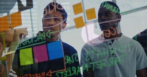 Young professionals brainstorming at glass wall with sticky notes and data overlays