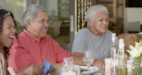 Senior couple laughing and chatting with African American woman at outdoor dinner on patio