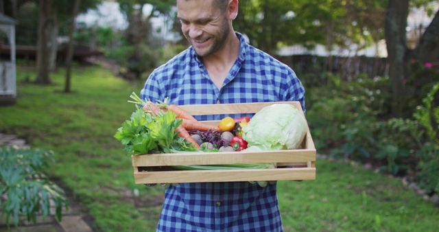 Smiling caucasian man standing in garden holding box of vegetables. spending free time at home.
