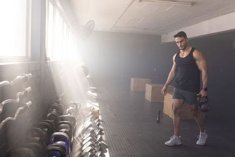 Sunlit asian athlete holding kettlebell walking through industrial gym