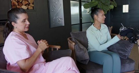 Nurse in scrubs and wellness host recording candid podcast conversation in cozy lounge