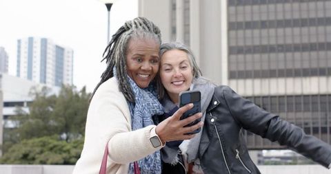 Mature diverse women taking selfie on urban plaza, smiling and enjoying city life together