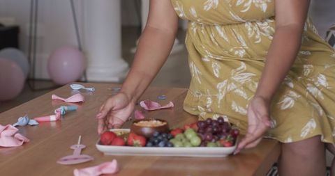 Woman in yellow floral dress serving fruit platter at home party