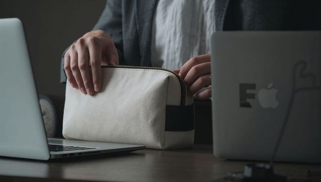 Unzipping canvas pouch between laptops on modern workspace desk