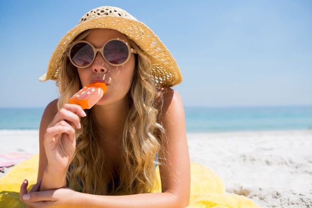 Portrait of beautiful woman eating popsicle while relaxing at beach on sunny day