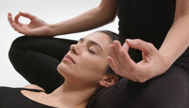 Woman reclining on partner lap while meditating in minimalist yoga studio, mudra calm
